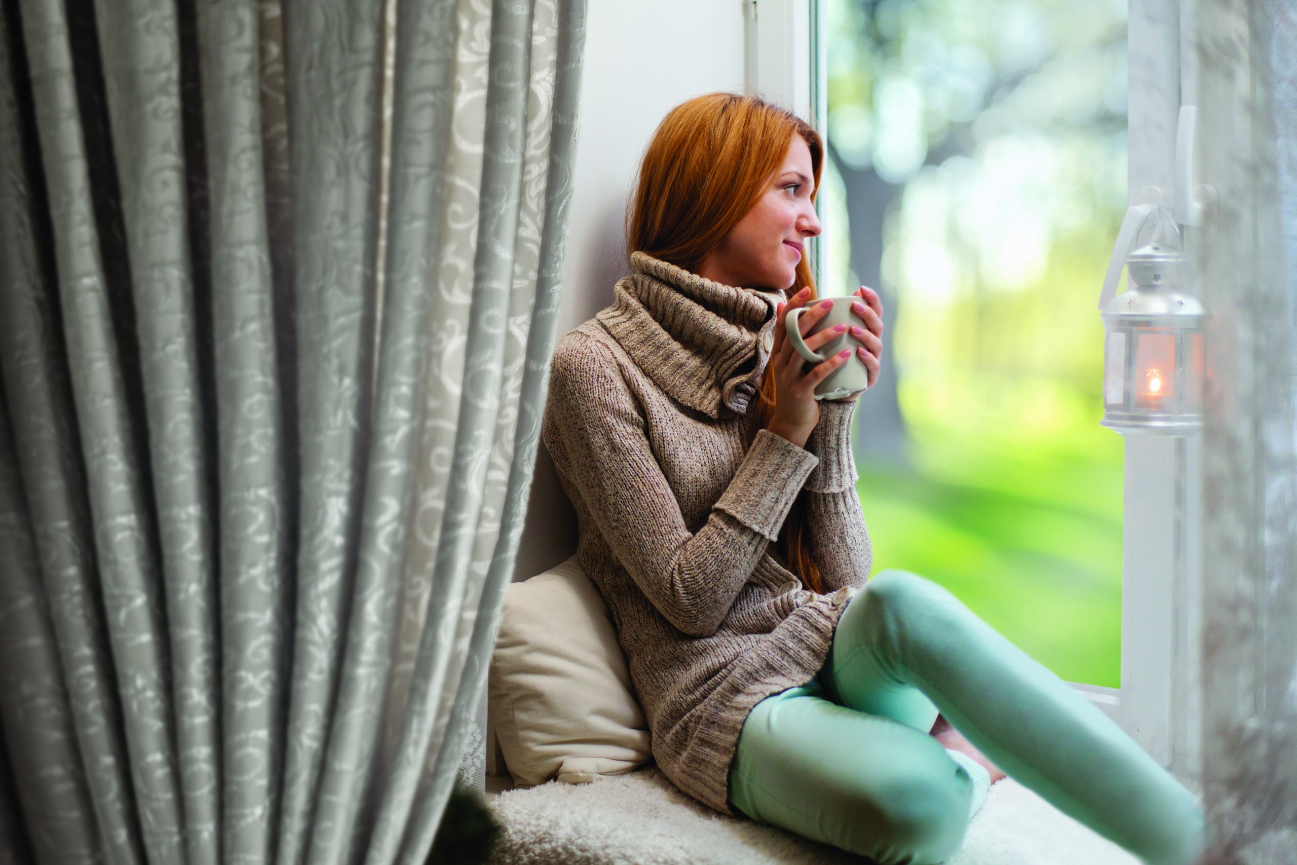 Young woman sitting by the window drinking hot coffee